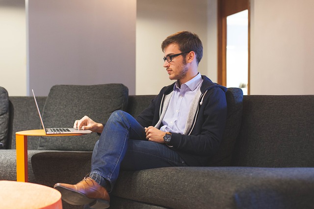 A young man sitting on a couch reading a guide for millennials renting in NYC