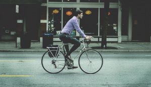 A man cycling in his jeans and a shirt.