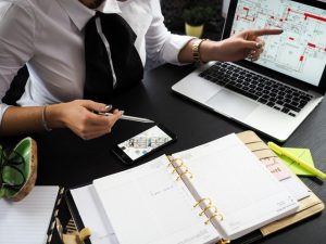 An expert working on the laptop and showing a house plan to a client.