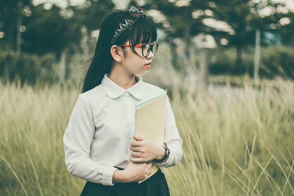 a little girl with glasses, holding her notebook.