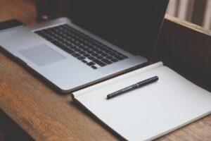 A laptop and a notebook on the desk.