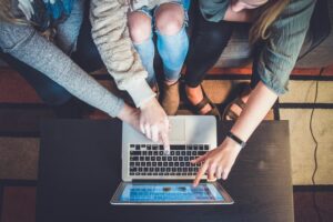 A group of friends pointing at the laptop and reading about how to budget your first apartment