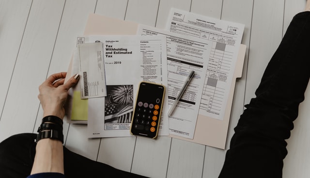 A person sitting on the floor and holding papers, a phone, and a pen